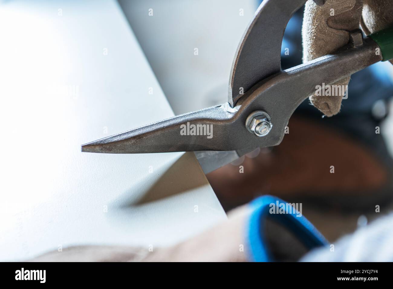 Ein Arbeiter schneidet vorsichtig eine dicke Materialplatte mit einer schweren Schere ab, während er in einer Werkstatt Schutzhandschuhe trägt. Stockfoto