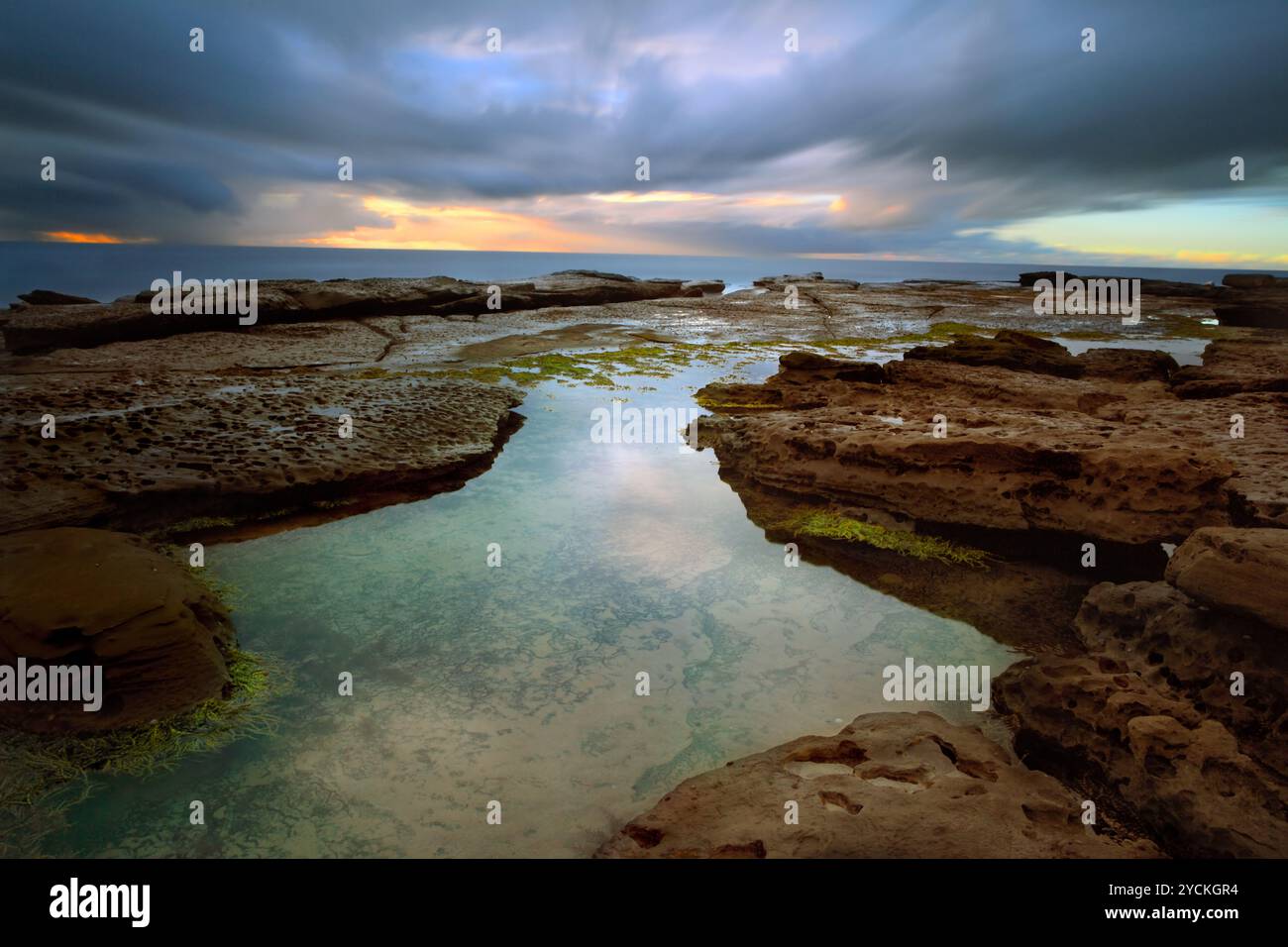 Stürmischer Sonnenaufgang über kleine Bucht mit Rockpool im Vordergrund Stockfoto