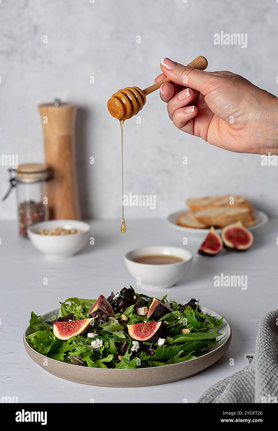 Lebensmittelfotografie von Salat mit Feigen und Fetakäse, Spinat, Salat, Honig, Pinienkernen, geröstetes Brot, gedeckter Tisch, Honig von Hand auf einen Salat gießen Stockfoto