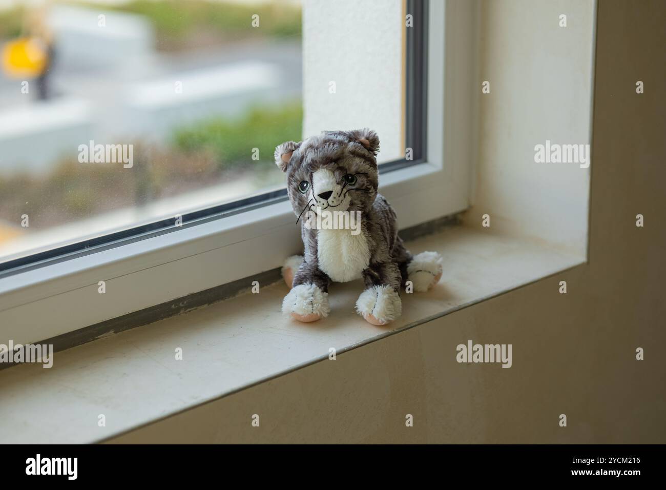 Weiches Plüschkatzenspielzeug auf Fensterbank in unvollendeter Wohnung mit Blick auf die Stadt. Konzept der Kindheit, des Komforts und des Wohnens in Renovierung Stockfoto