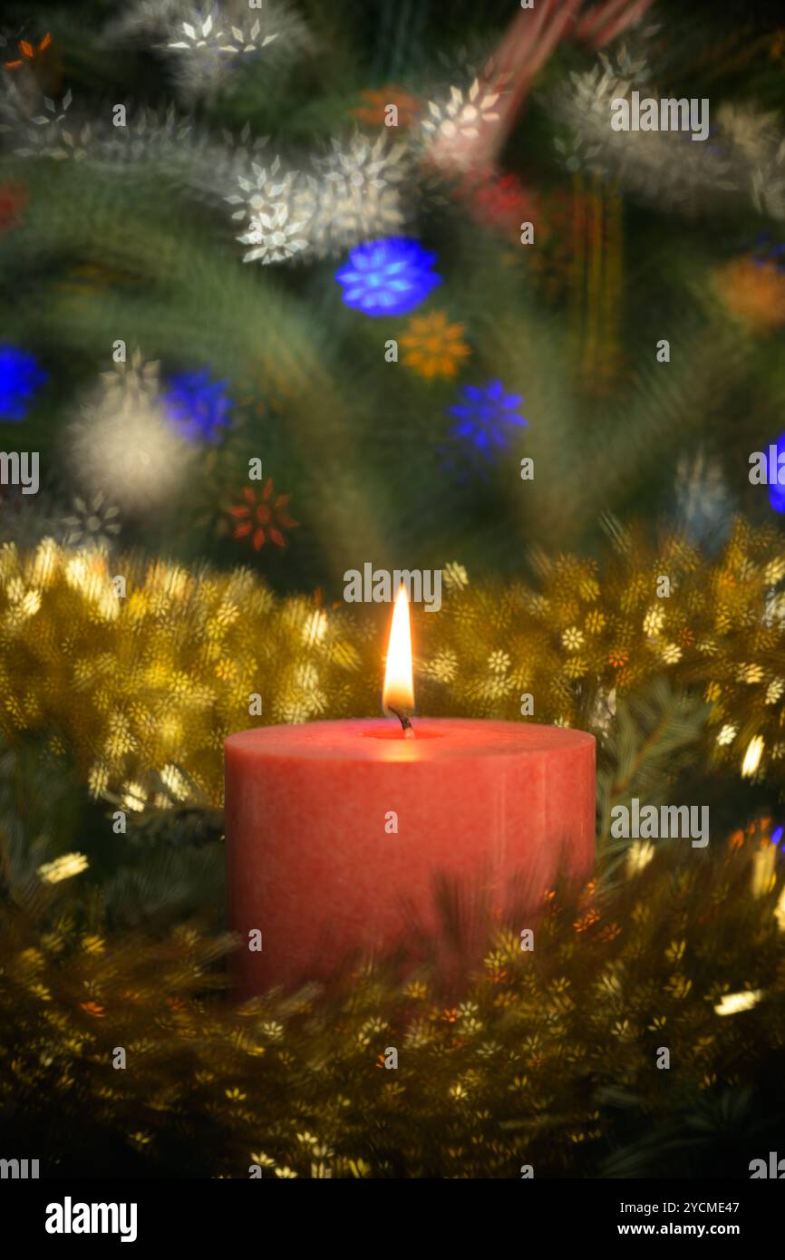 Rote Kerze umgeben von Weihnachtskranz und Lametta, mit Schneeflocken-förmigen Bokeh-Highlights Stockfoto