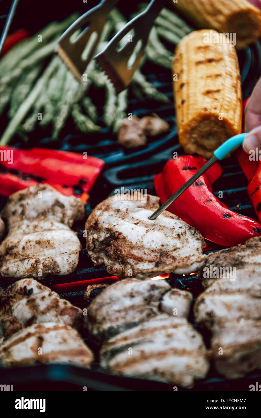 Köstliches gegrilltes Hähnchenfleisch mit Gemüse, Spargel, Paprika und Maiskolben auf Grill mit Rauch und Flamme. Hühner auf sichere Lebensmittel prüfen Stockfoto