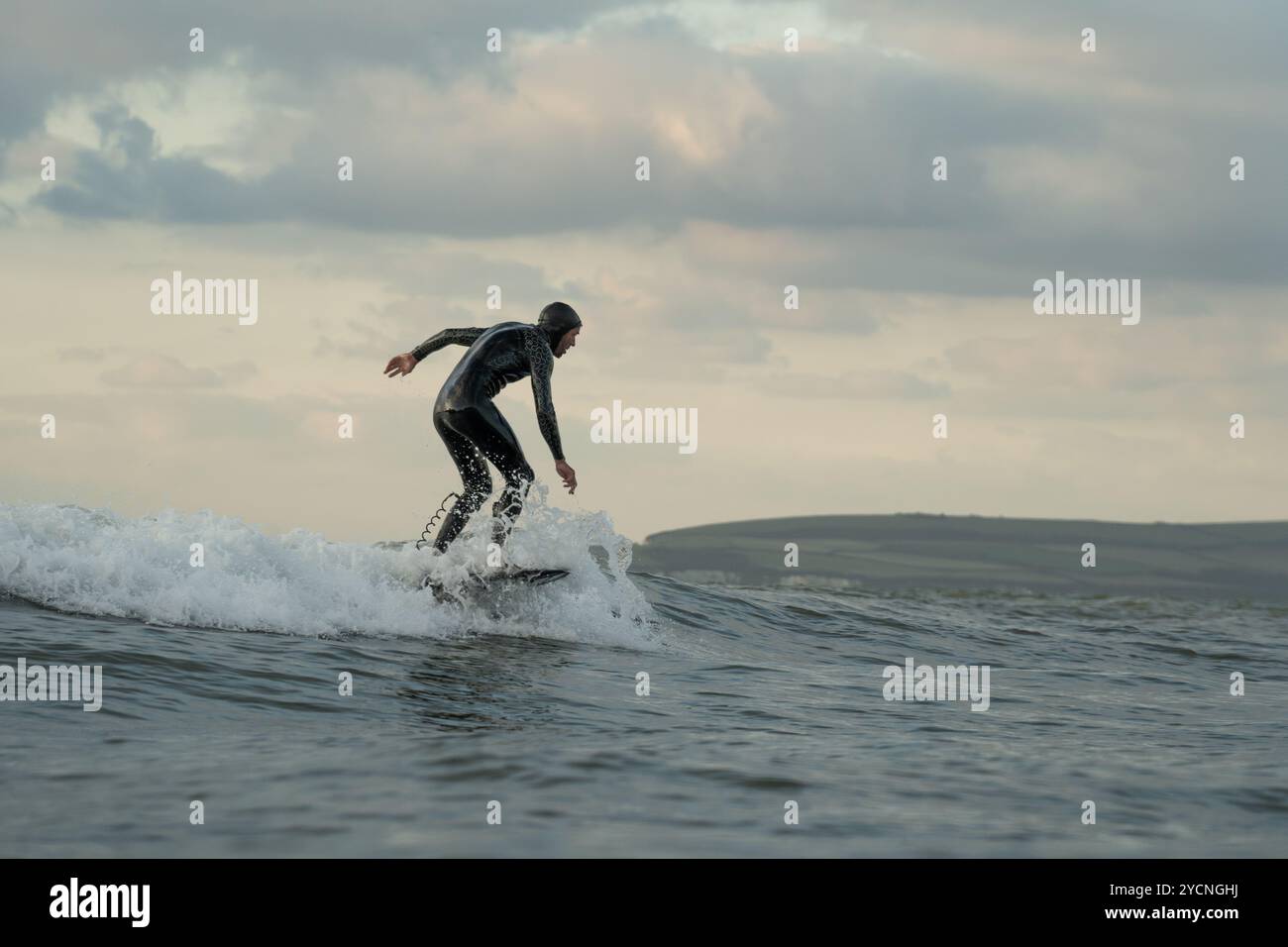 Ein junger Mann in einem schwarzen Neoprenanzug reitet auf einem Tragflächenboot-Surfbrett in kleinen Wellen vor dem Strand von Bourenmouth. Stockfoto