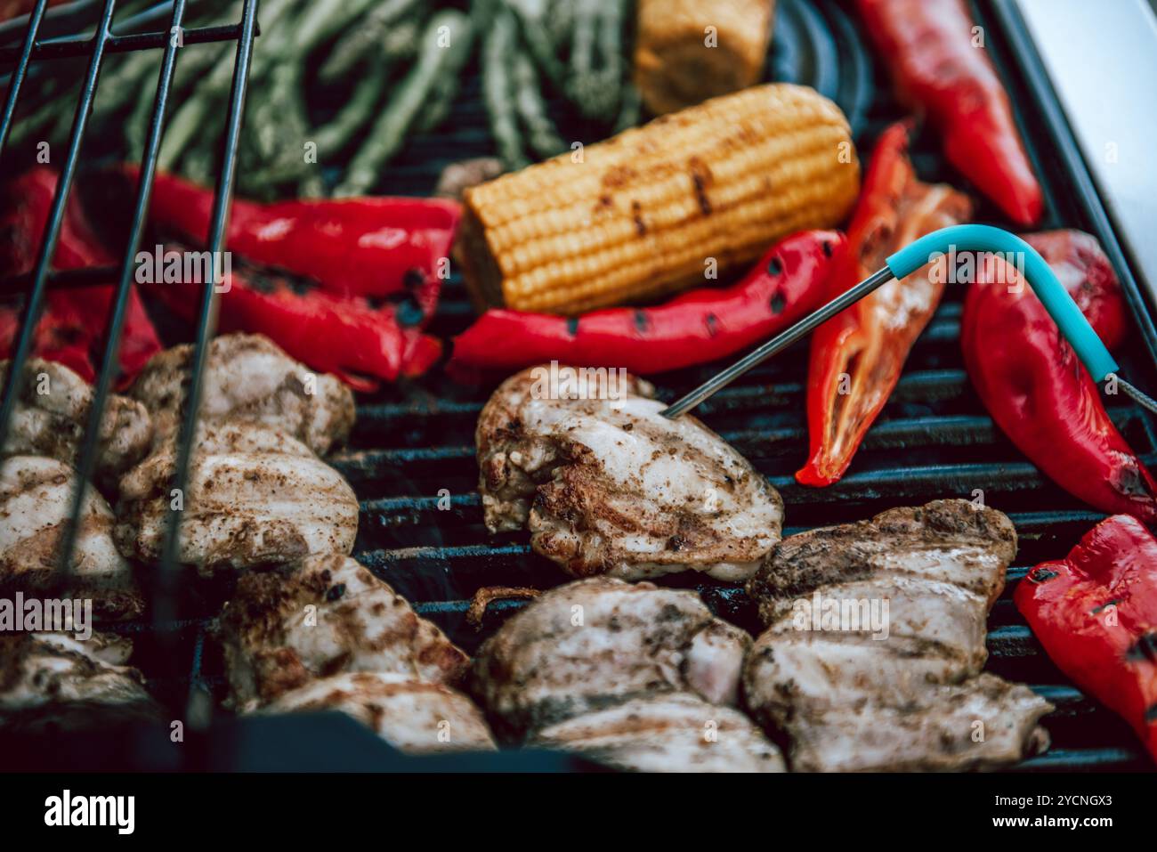 Köstliches gegrilltes Hähnchenfleisch mit Gemüse, Spargel, Paprika und Maiskolben auf Grill mit Rauch und Flamme. Hühner auf sichere Lebensmittel prüfen Stockfoto