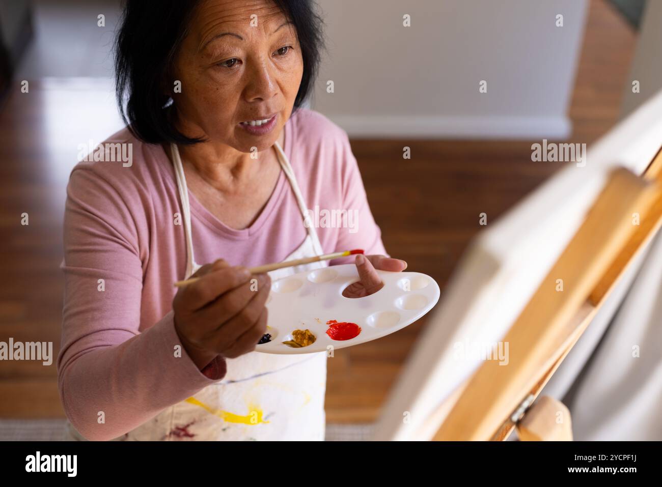 Ältere asiatische Frau, die zu Hause malte, mit Schwerpunkt auf der Gestaltung von Kunst mit Palette Stockfoto