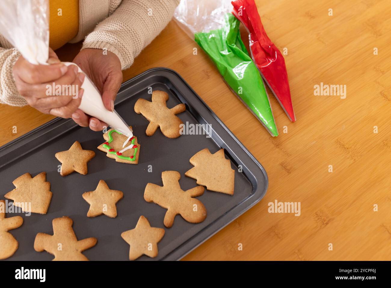 Asiatische Seniorin, die weihnachtskekse mit Glasur auf Backblech dekoriert, zu Hause Stockfoto