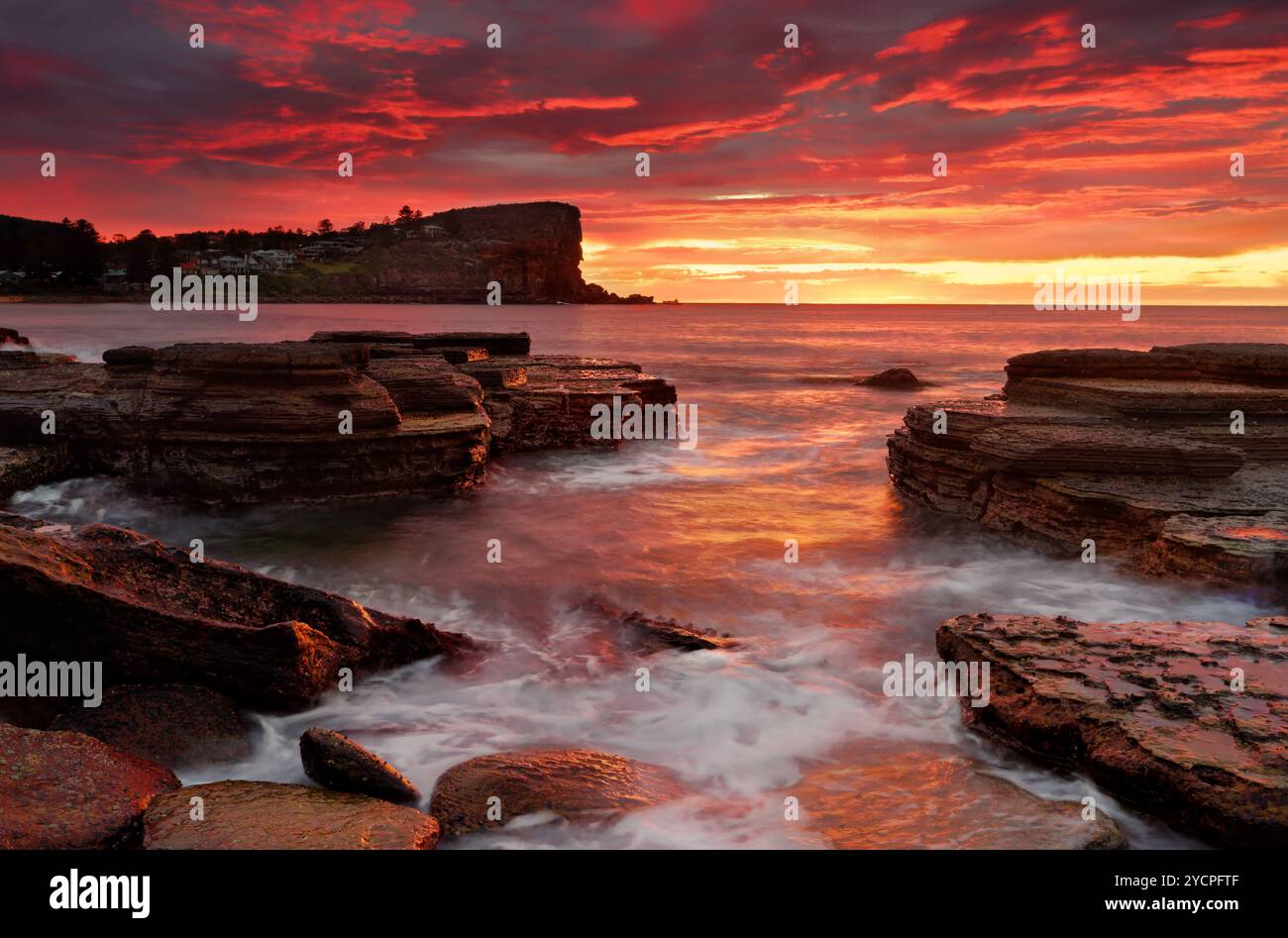 Feurige Farben des Sonnenaufgangs decken die Wolken und den Himmel in sattem, flammendem Rot und Gelb. Malerische Ausblicke vom südlichen Felssockel bei Avalon auf Sydne Stockfoto