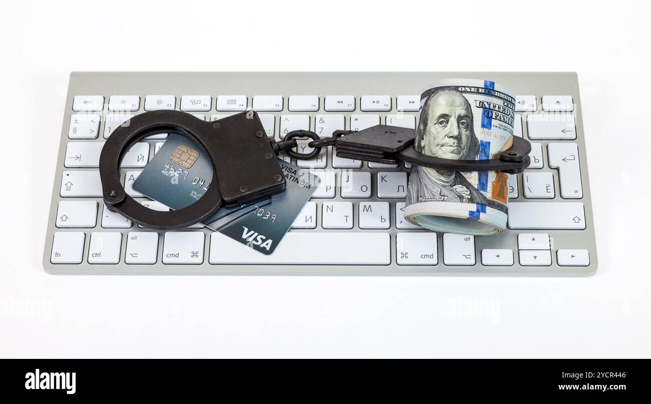 Stahlhandschellen, Kreditkarte und Dollarscheine liegen auf einer Computertastatur auf weißem Hintergrund Stockfoto
