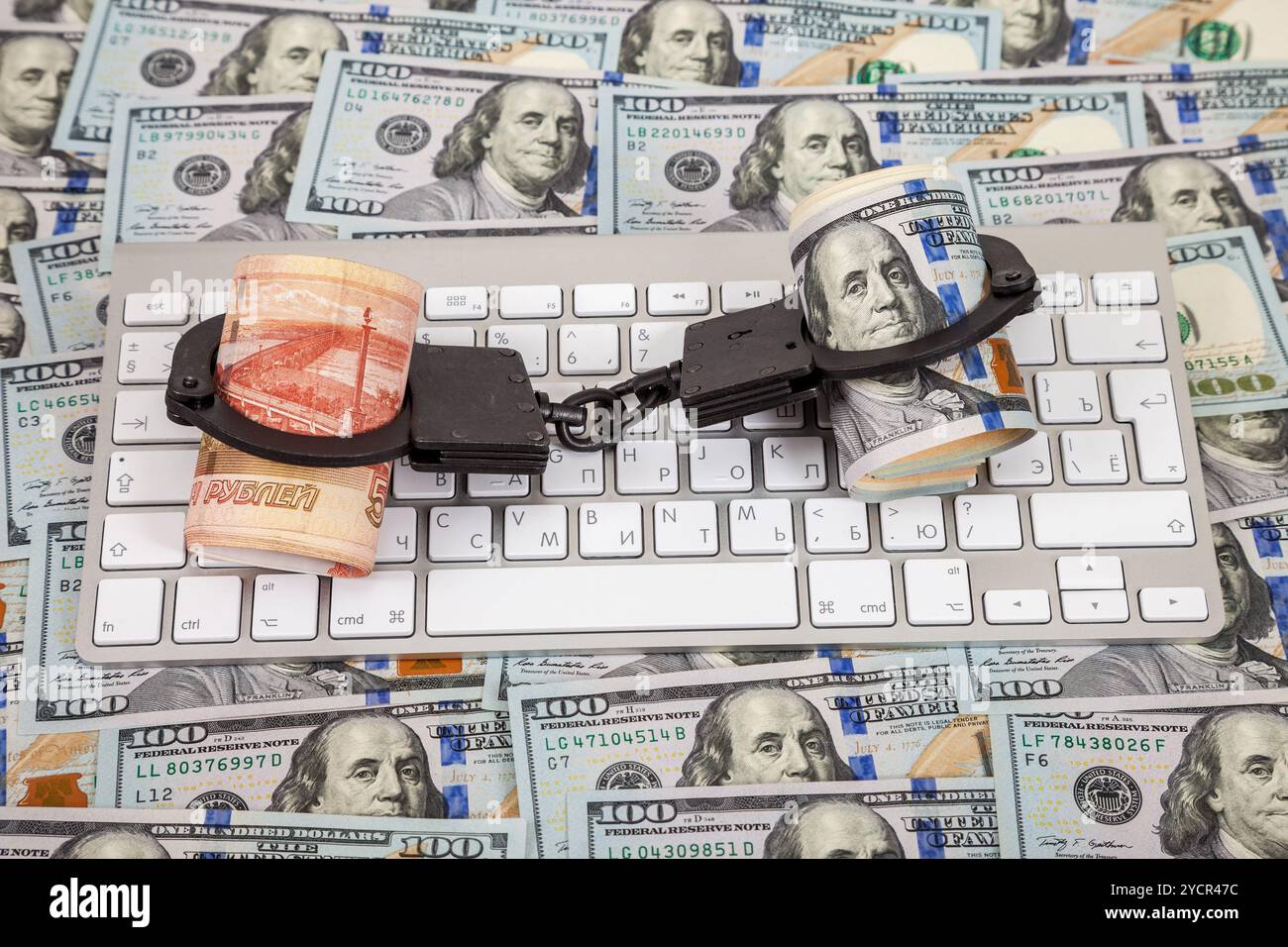 Stahlhandschellen, Rollen russischer Rubel und Dollar, die auf einer Computertastatur liegen, auf dem Hintergrund von Dollars Stockfoto