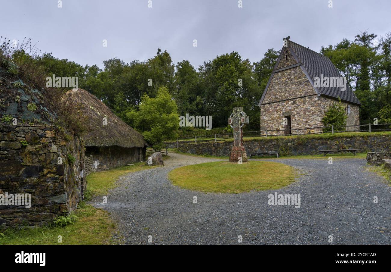 Wexford, Irland, 18. August 2022: Blick auf ein früh rekonstruiertes christliches Kloster im Irish National Heritage Park mit einem großen keltischen Kreuz Stockfoto