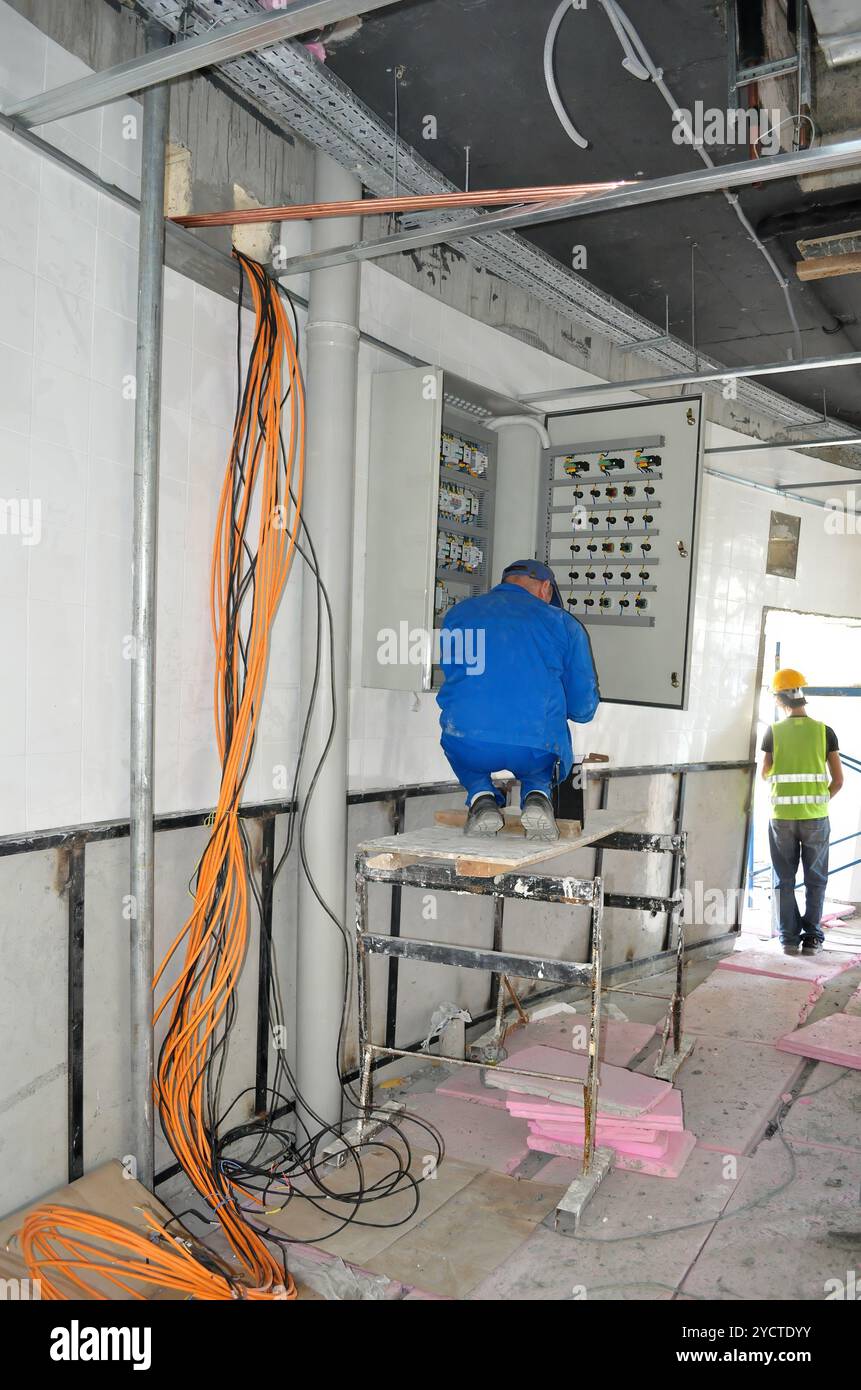 Ein Elektriker führt Verdrahtungsaufgaben an einem Verteiler auf einer aktiven Baustelle durch. Stockfoto