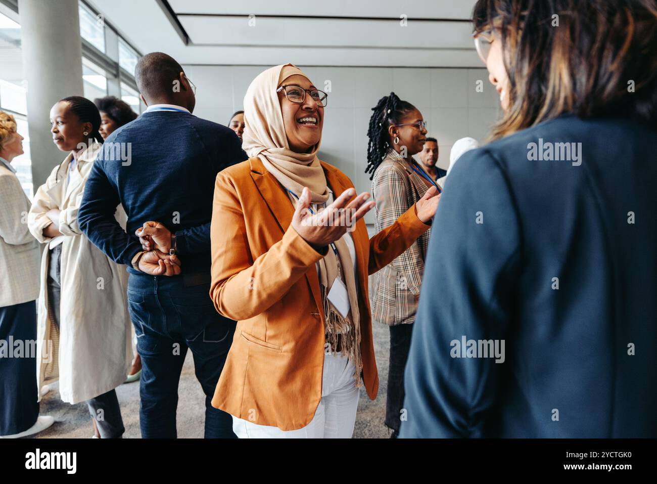 Lächelnde muslimische Geschäftsfrau, die sich bei einem Networking-Event mit Kollegen teilt und mit ihnen spricht. Professionelle Frauen, die sich in einem lebhaften Gespräch unterhalten. Stockfoto Lächelnde muslimische Geschäftsfrau, die sich bei einem Networking-Event mit Kollegen teilt und mit ihnen spricht. Professionelle Frauen, die sich in einem lebhaften Gespräch unterhalten. Stockfoto