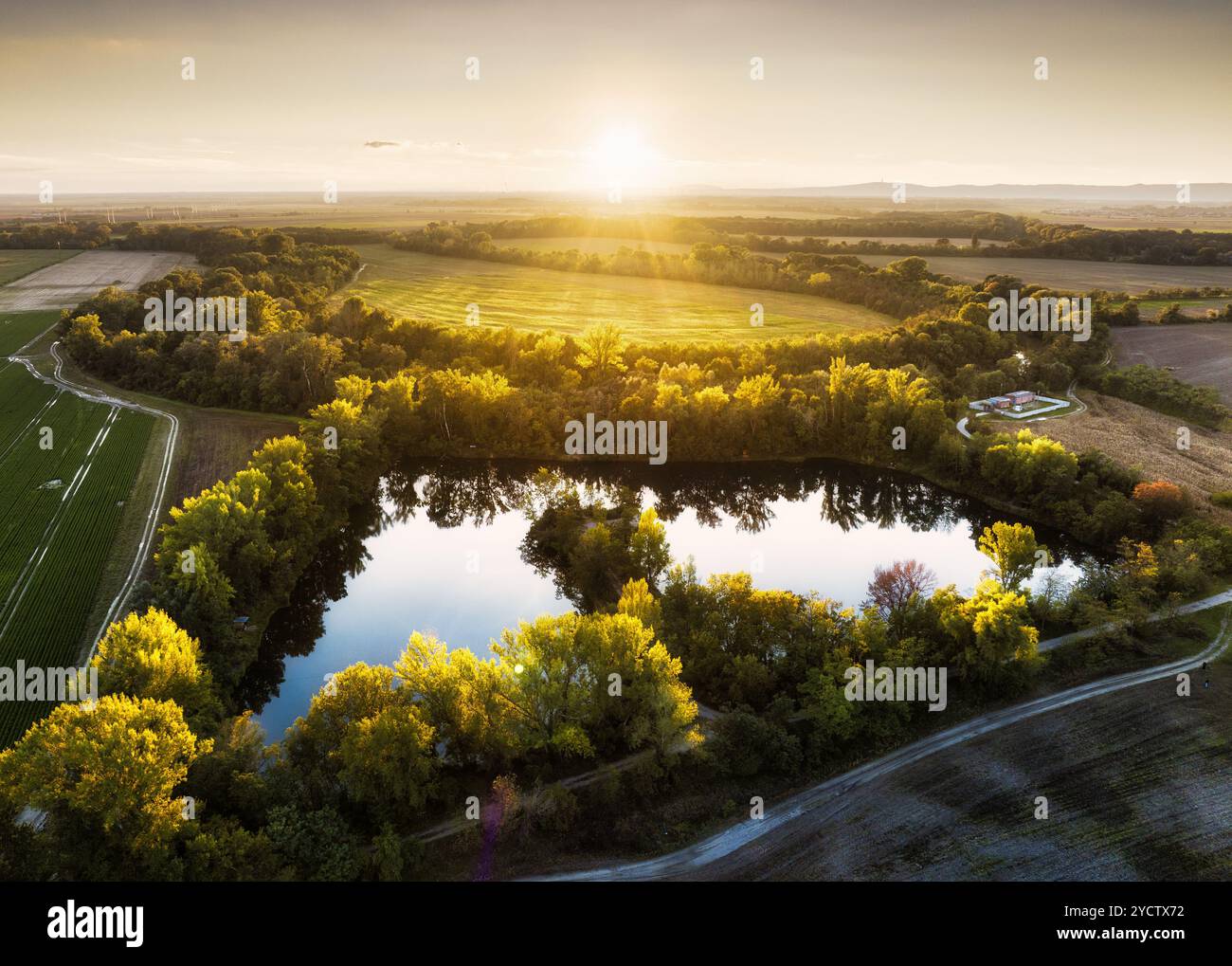 See im ländlichen Raum bei Sonnenuntergang, Drohnenblick. Ländliche Landschaft mit Seen. Teich auf dem Land mit Feldern. Grünes Farmfeld und Ackerland auf dem Land. Dorf in Stockfoto
