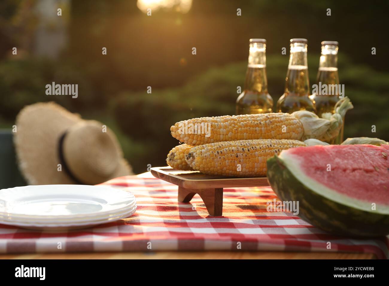 Frische Wassermelone, Mais, Teller und Getränkeflaschen auf dem Tisch im Garten Stockfoto