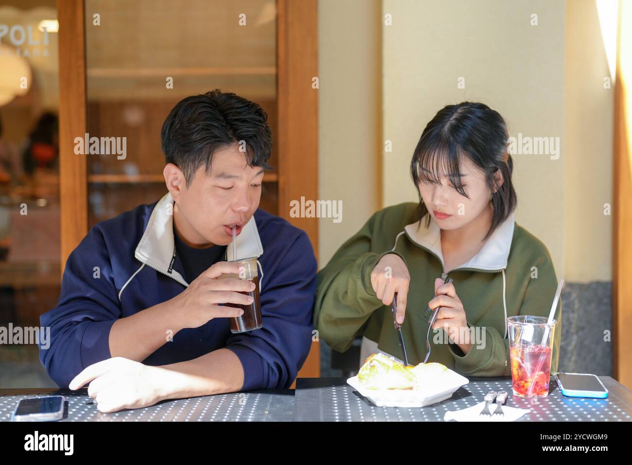 Mann und Frau sitzen an einem Tisch und essen und trinken. Der Mann trinkt eine Limonade und die Frau isst ein Stück Kuchen Stockfoto