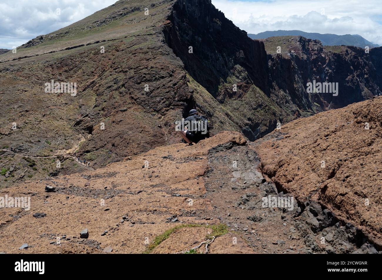 Ein Wanderer nimmt sich einen Moment Zeit, um sich am Rande einer Klippe mit Blick auf das zerklüftete Gelände von Vereda da Ponta de São Lourenco auszuruhen Stockfoto