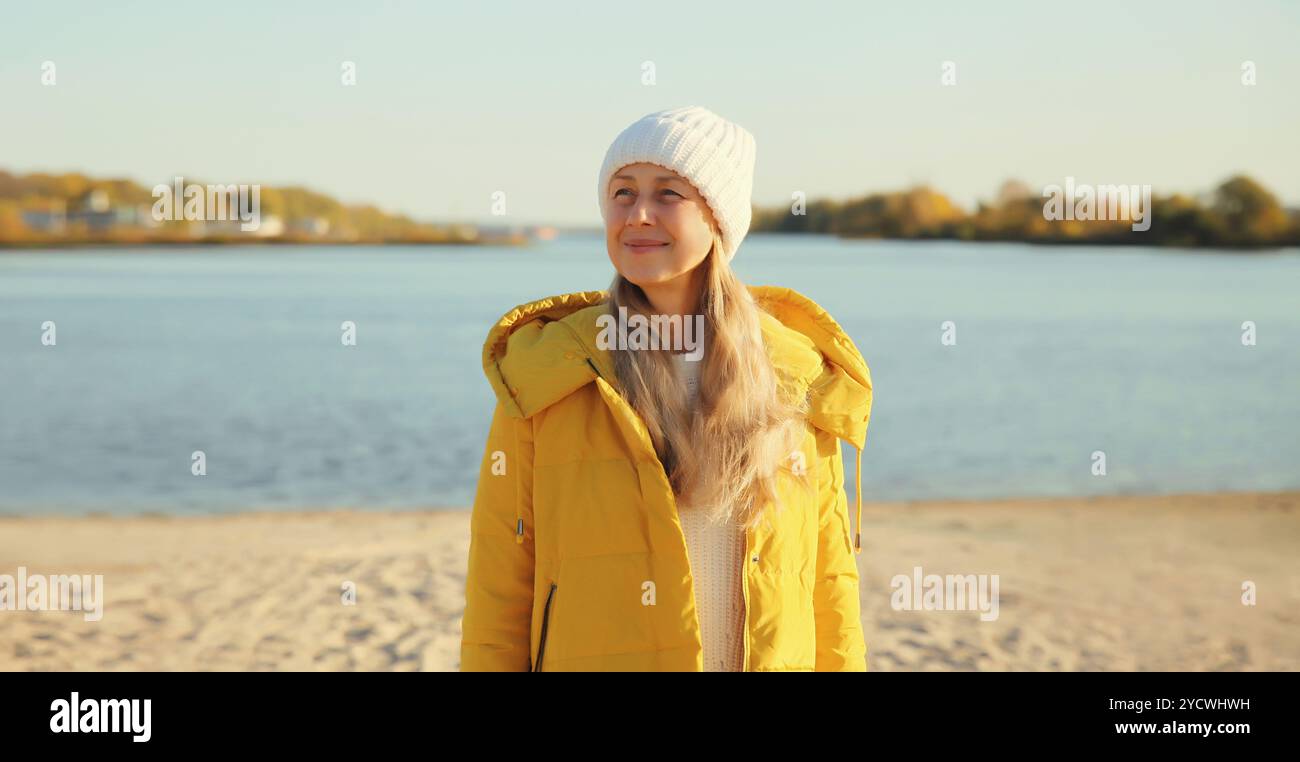 Reisende Frau blickt weg auf sonnigen Strand, genießt erstaunliche Landschaft, warmes Wetter, trägt Hut, gelbe Jacke, an der Meeresküste, Natur im Hintergrund Stockfoto