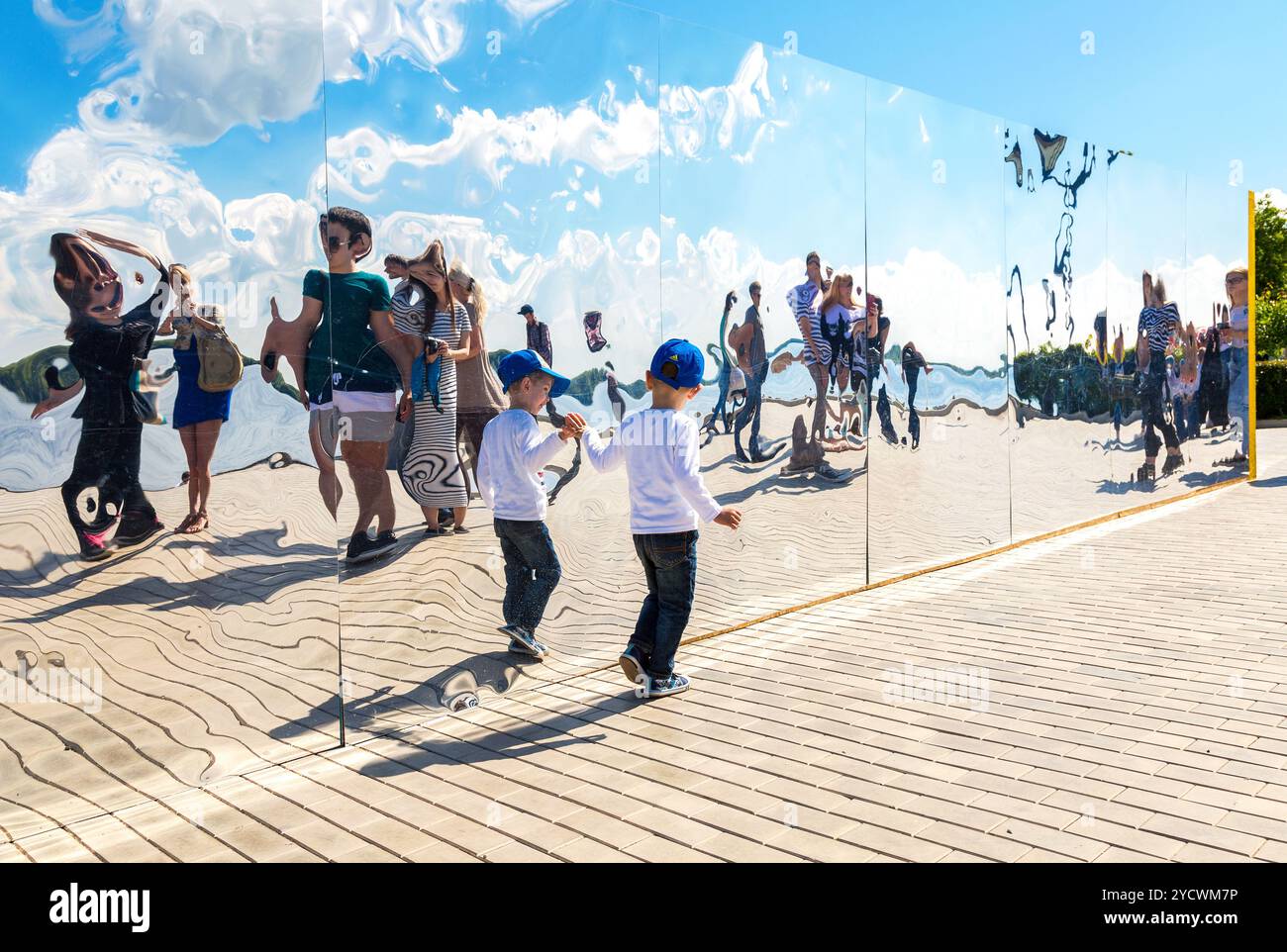 Kleiner Junge in der Nähe des riesigen Edelstahlspiegels im Stadtpark an sonnigen Sommertagen Stockfoto