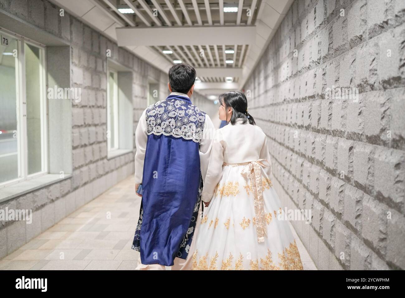 Mann und Frau gehen den Flur entlang. Der Mann trägt eine blaue Jacke und die Frau ein weißes Kleid Stockfoto