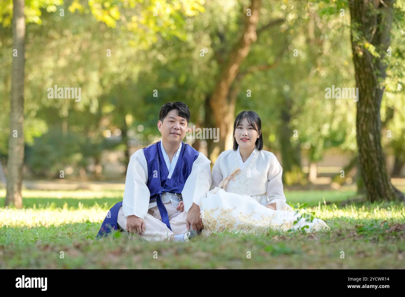 Ein koreanisches Paar in den 30ern und eine Frau in den 20ern blicken in einem grünen Park, der von Bäumen umgeben ist, während sie Hanbok in Seoul tragen Stockfoto