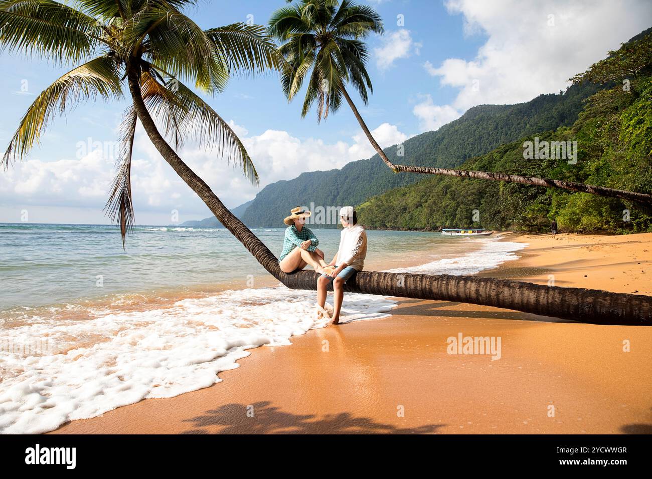 Mutter und Sohn, Touristen, sitzen auf einer Palme, die über dem orangefarbenen Sandstrand hängt, umgeben von Regenwald auf der Insel Labengki, Sulawesi, Indonesien Stockfoto