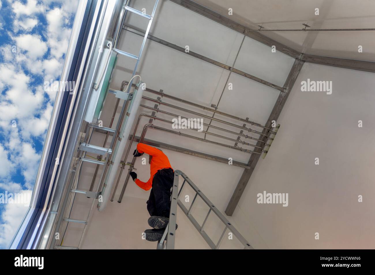 Edelstahlrohre, die von einem afroamerikanischen Arbeiter in der Decke installiert wurden, Druckluft- und Elektrorohre Stockfoto