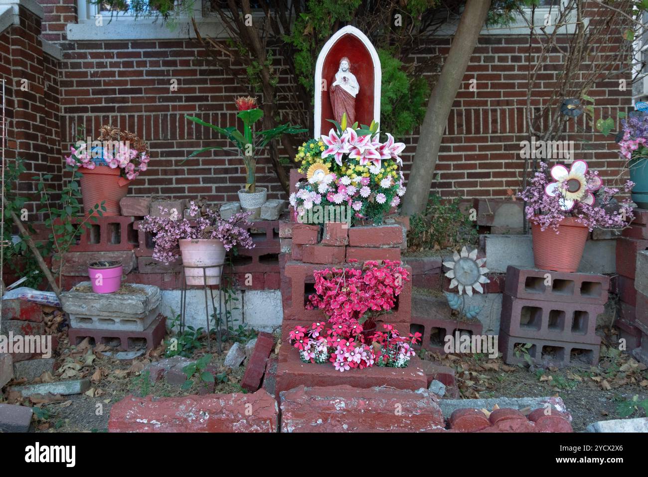 Ein Garten im Freien in Corona mit einer religiösen Statue, echten und künstlichen Pflanzen und Ziegeln. In Queens, New York. Stockfoto