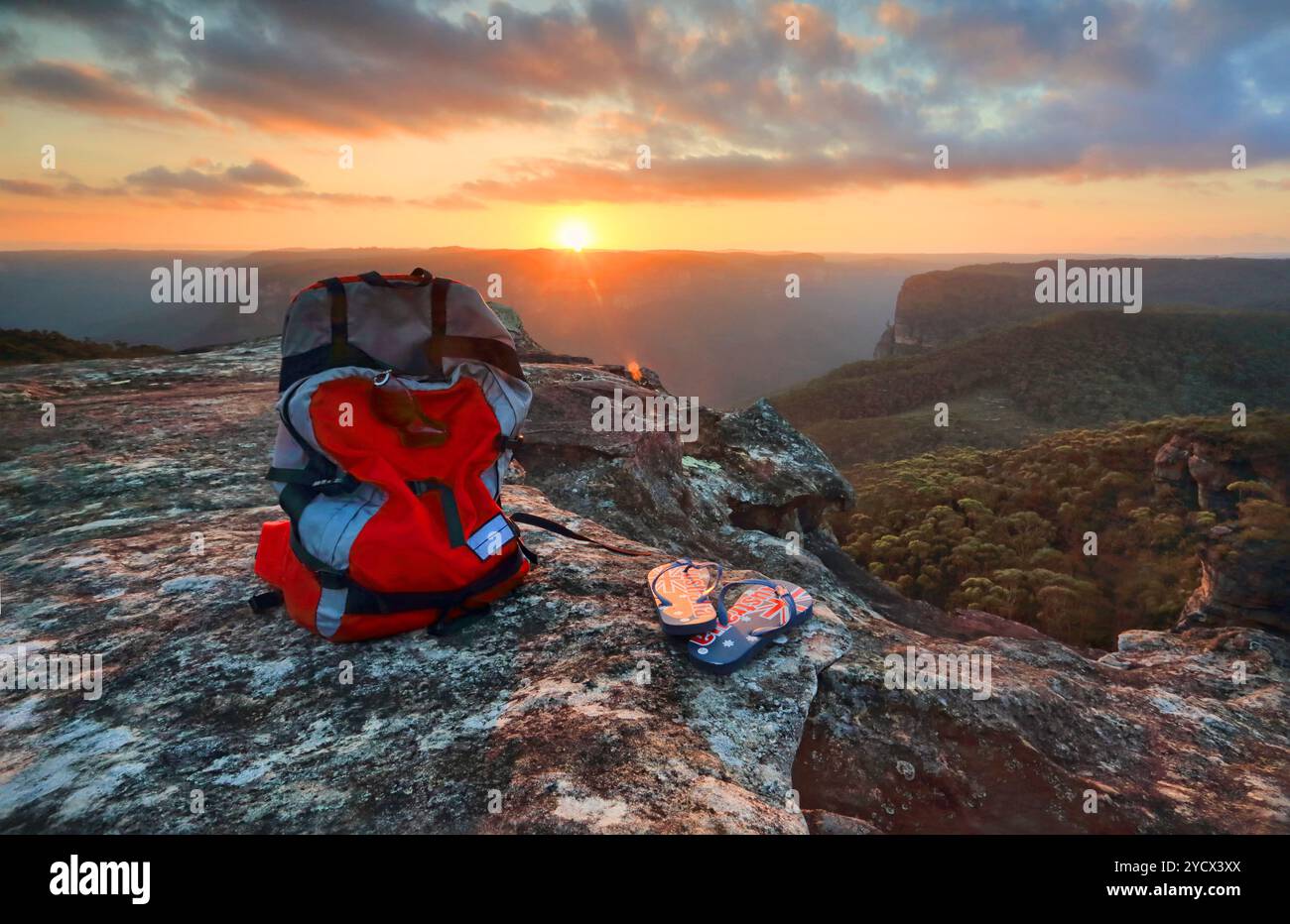 Sonnenuntergang von einem Felsvorsprung der Explorers Range, Blue Mountains Australien. Ein Rucksack und Tangas mit australischer Flagge sind das letzte Licht Stockfoto