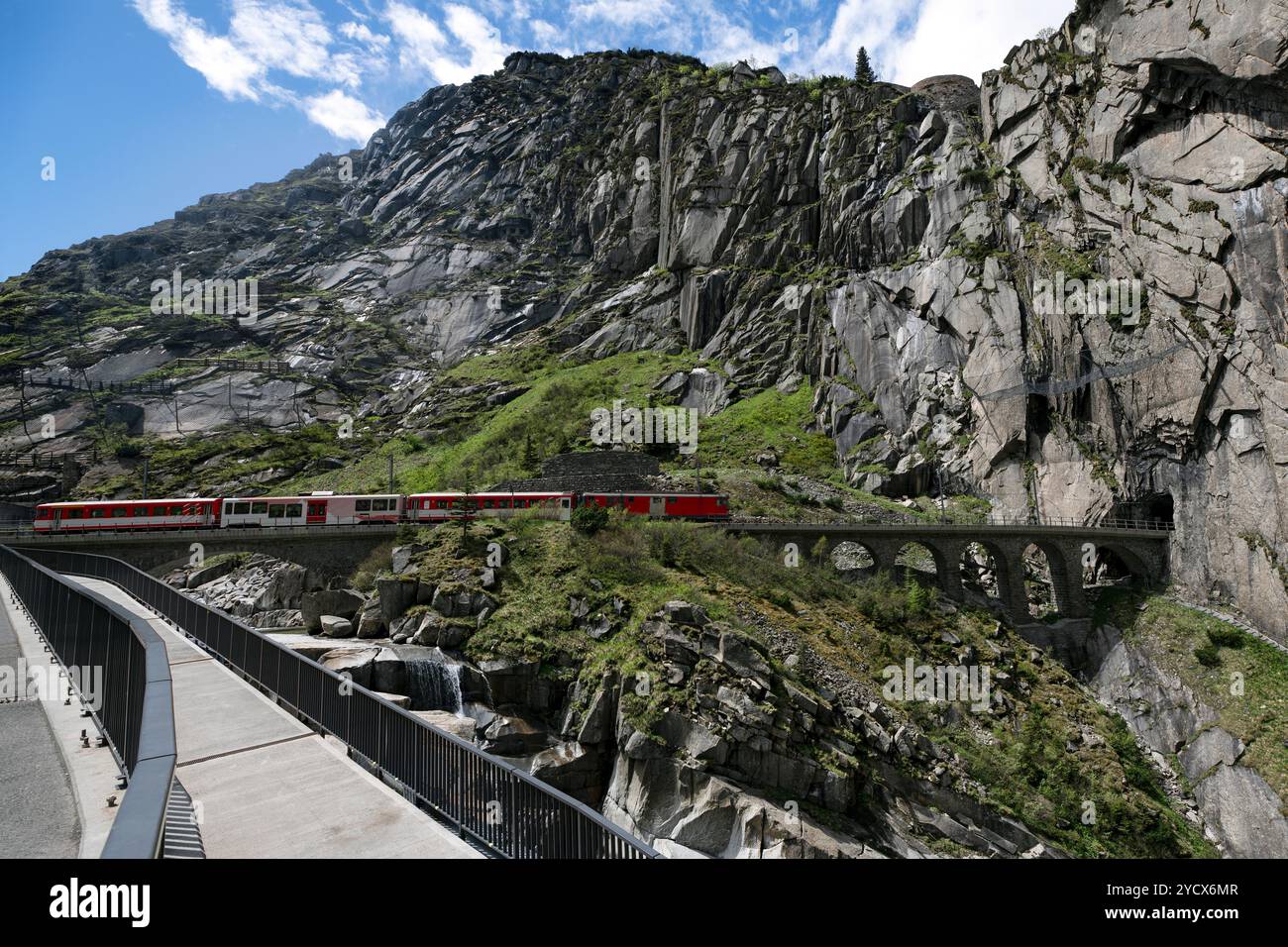 Der Zug fährt durch eine Viadukt, die sich über einen bergigen Bach erstreckt, in Richtung Tunnel Stockfoto