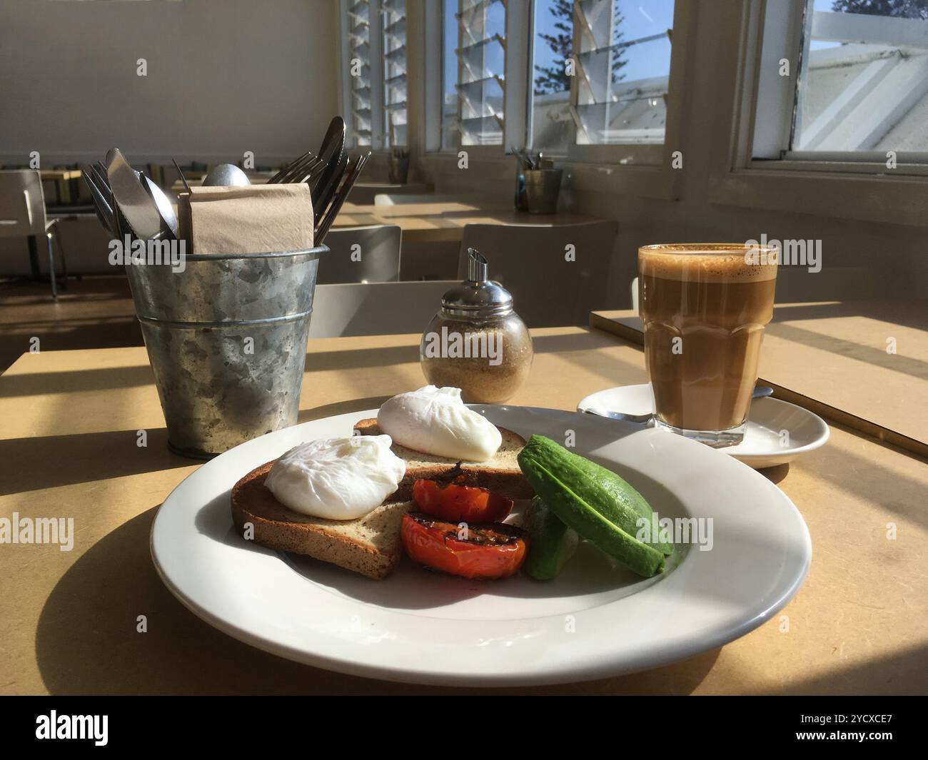 Pochierte Eier, Avocado und gegrillte Tomaten mit Latte im Café Stockfoto
