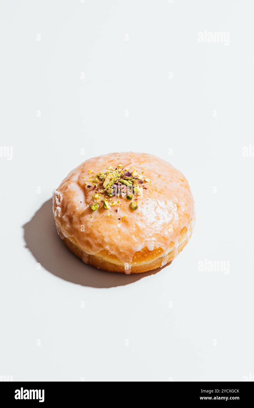 Ein glasierter Donut mit zerstoßenen Pistazien sitzt auf einer hellen Oberfläche und zeigt ihre glänzende, goldene Textur Stockfoto
