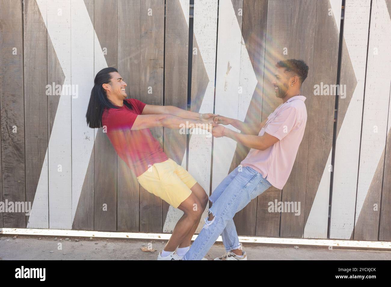 Ein fröhliches schwules Paar tanzt fröhlich in einer verspielten Pose in einer urbanen Umgebung und zeigt die Vielfalt und den Geist der LGBTQIA+ Community Stockfoto