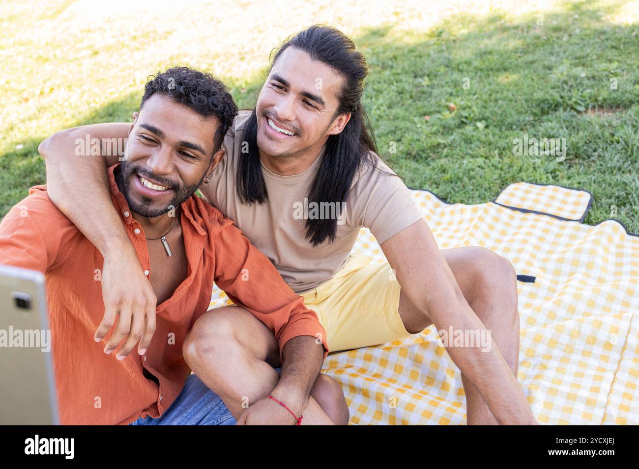 Zwei schwule Männer lateinamerikanischer und afroamerikanischer Abstammung teilen einen freudigen Moment, während sie ein Selfie in einem Park machen und den Charme von LGBTQIA+ Relationsh unterstreichen Stockfoto