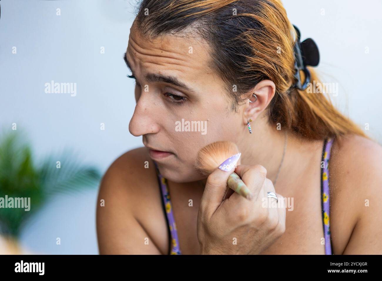 Eine fokussierte Transfrau schminkt sanft mit einem Pinsel und fängt einen Moment der persönlichen Pflege und des Identitätsausdrucks ein Stockfoto