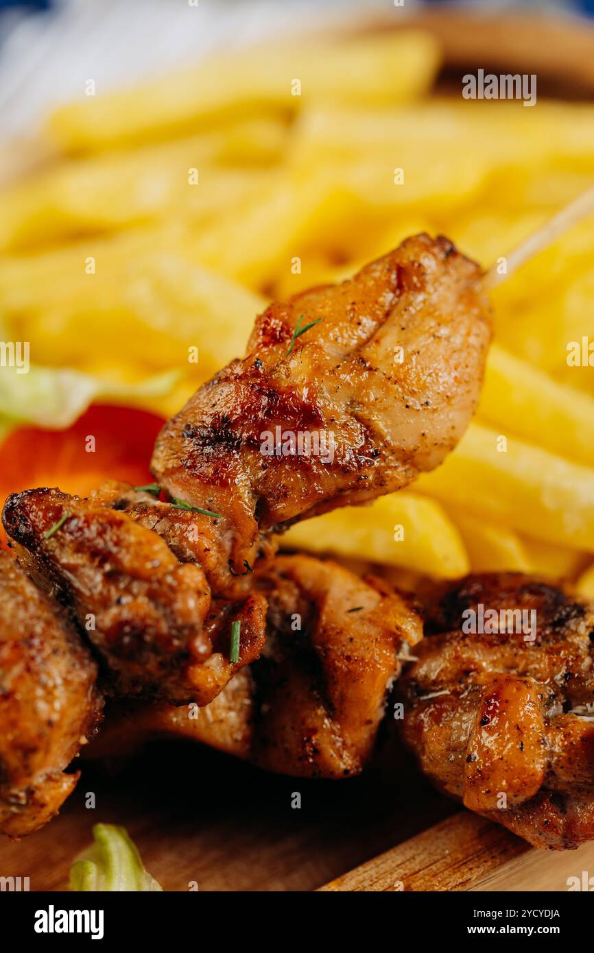 Nahaufnahme saftiger gegrillter Hähnchenspieße mit knusprigen Pommes Frites, perfekt zum Mittag- oder Abendessen Stockfoto