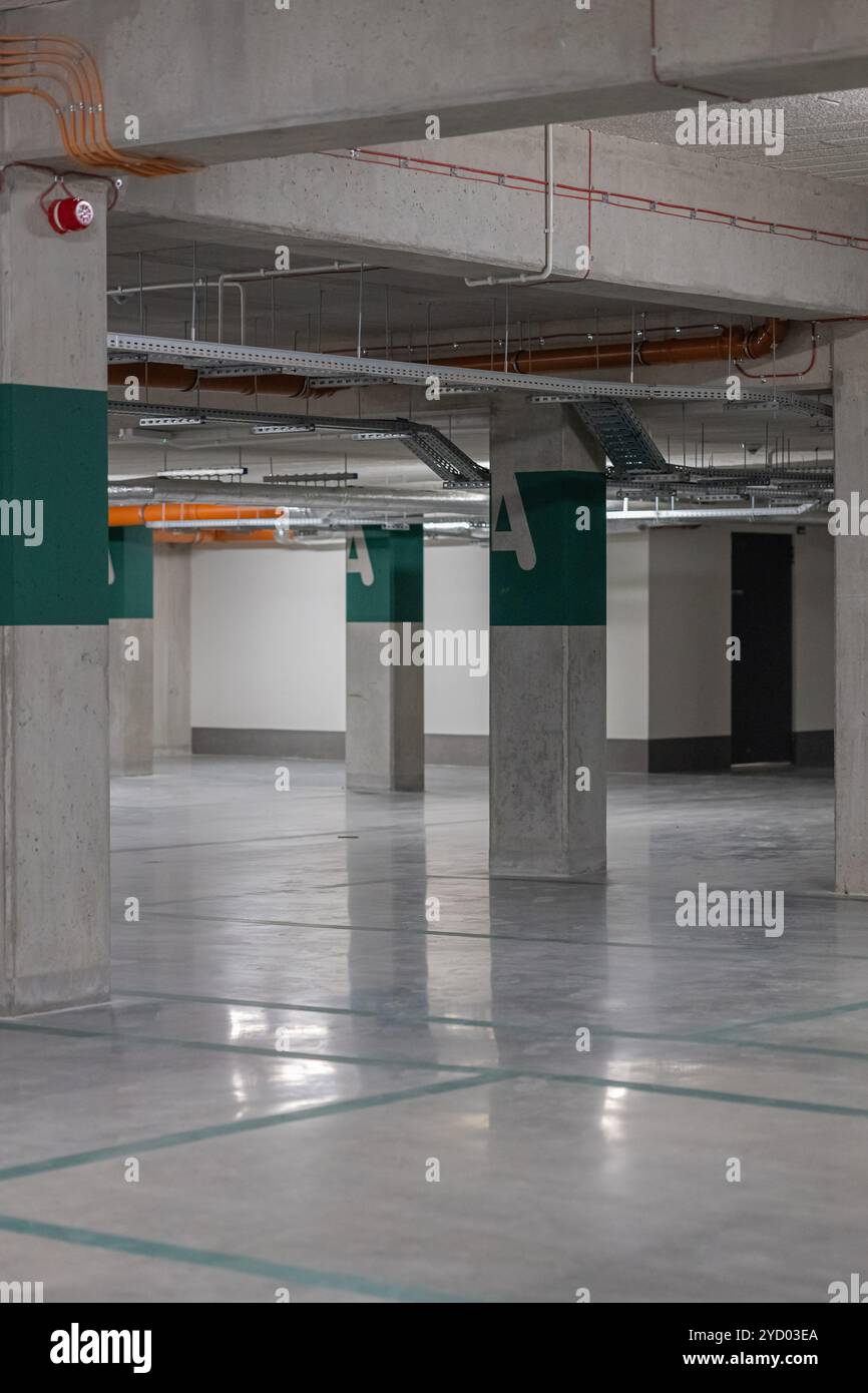 Moderner Tiefgaragenplatz mit Betonsäulen und Lüftungssystem, Leerraum mit reflektierendem Boden und Markierungen Stockfoto