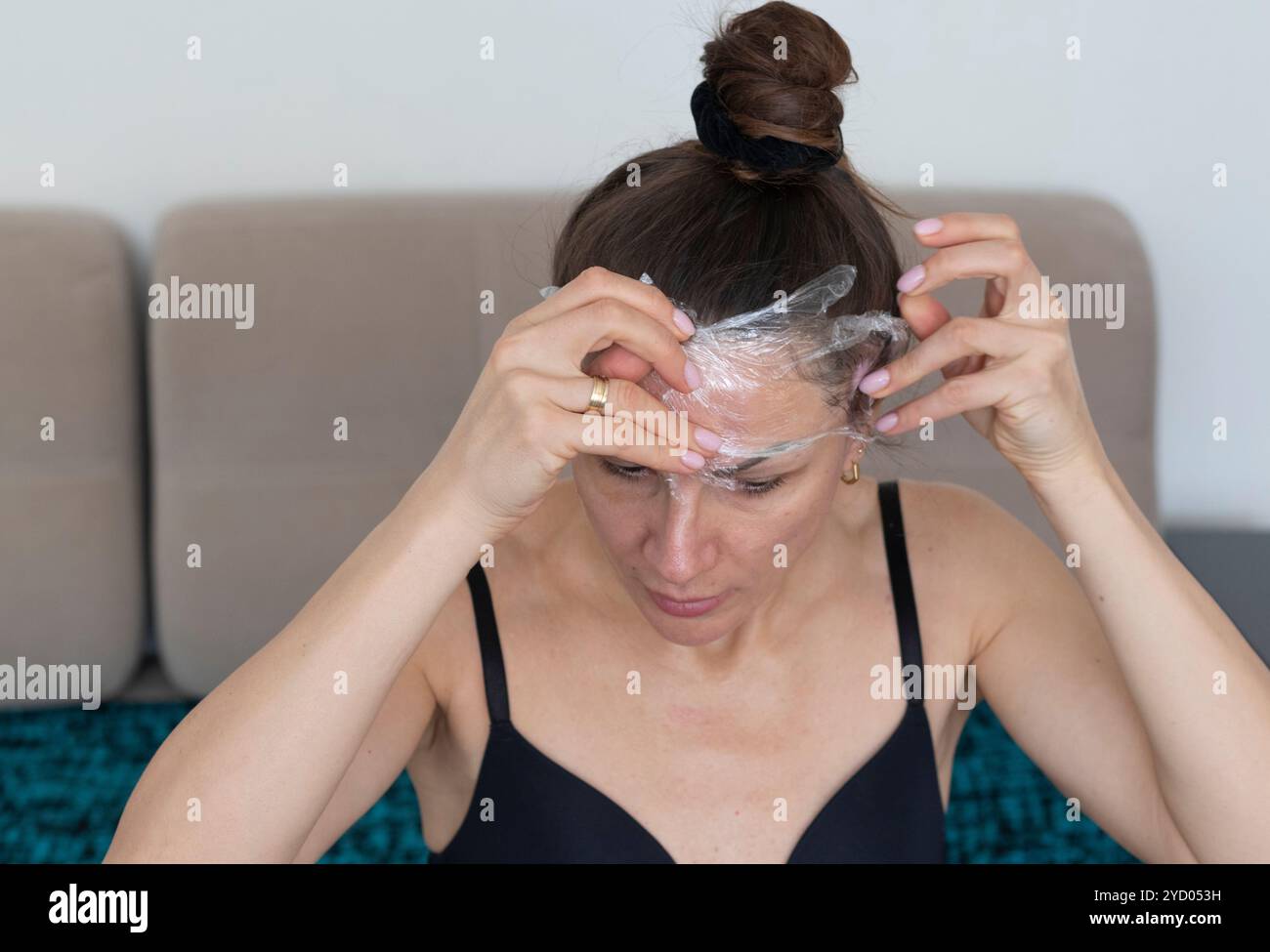 Frau, die ihr Gesicht und ihren Hals mit einer Frischhaltefolie als Hautpflegetherapie umwickelt Stockfoto