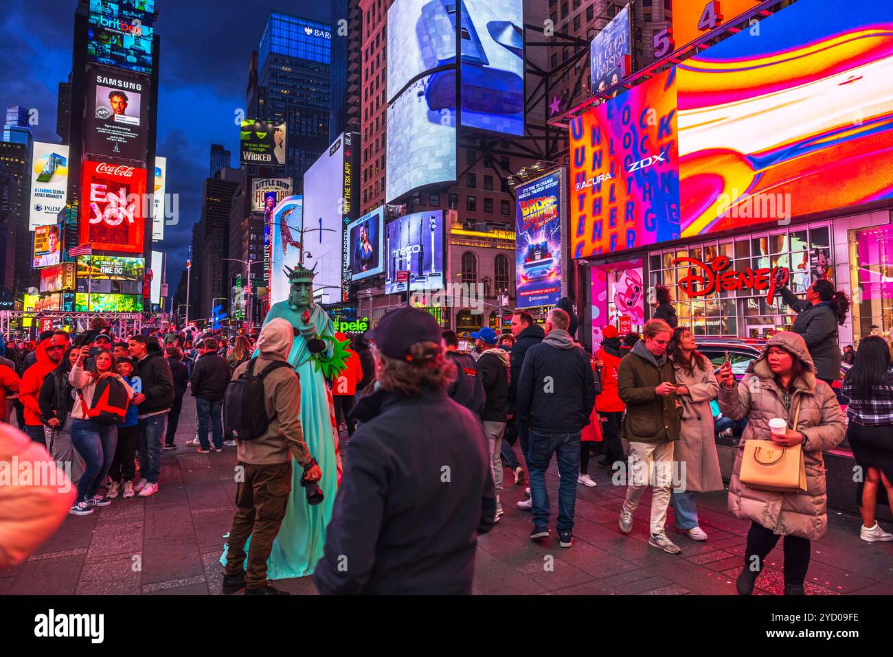 Pulsierende Touristenszene am Times Square, New York City, mit hell beleuchteten Reklametafeln und Darstellern, die als Freiheitsstatue verkleidet sind. New York. USA. Stockfoto