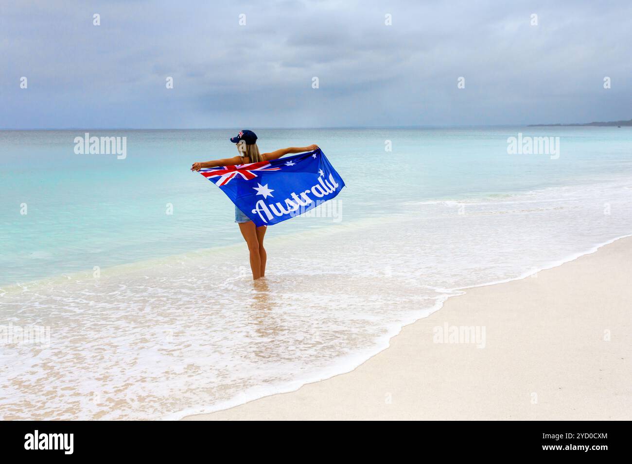 Frau am atemberaubenden weißen Sandstrand, die mit Stolz und Freude die australische Flagge hält Stockfoto