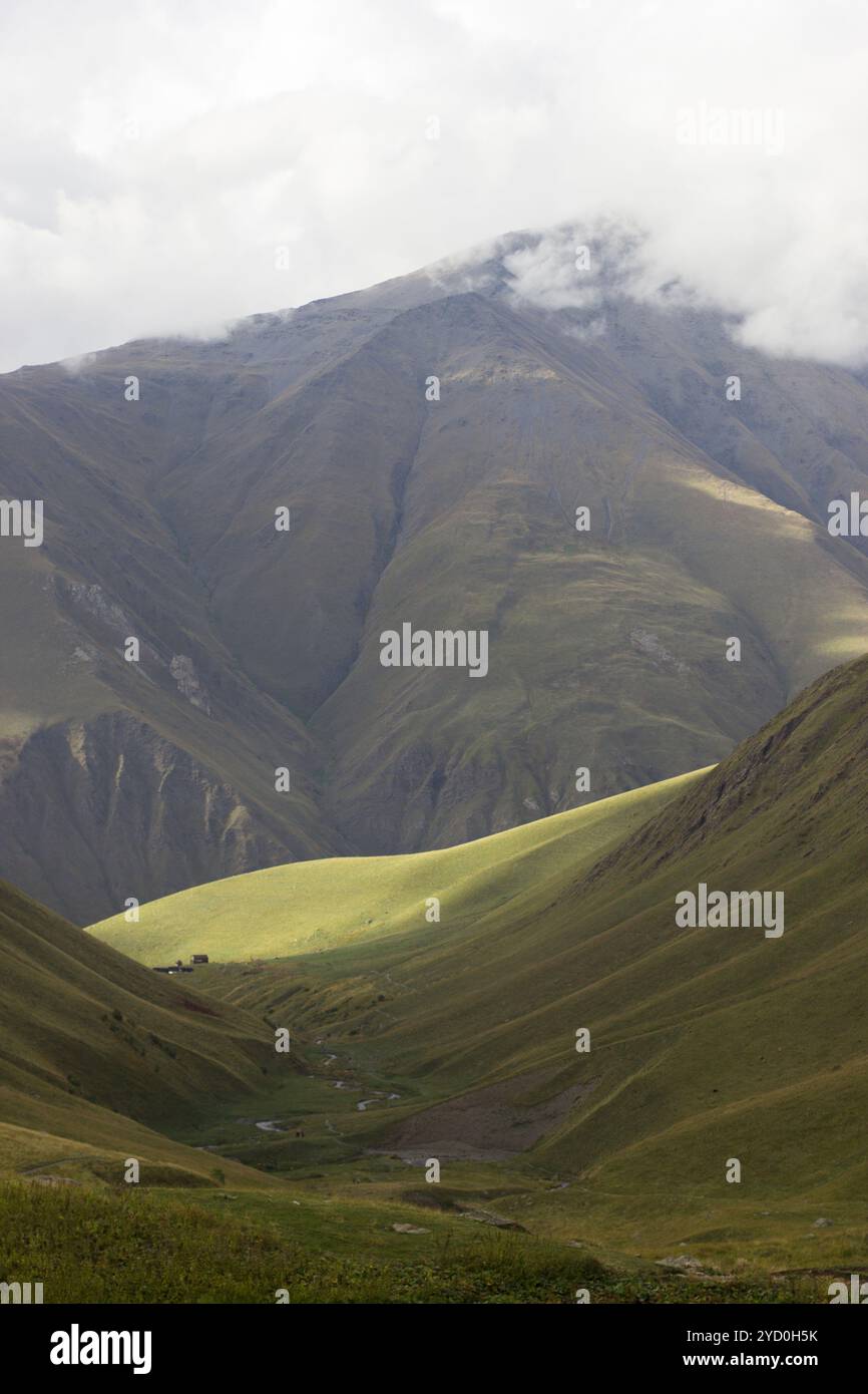 Ein ruhiges und ausgedehntes Bergtal, gekennzeichnet durch sanfte grüne Hügel und steile Berghänge im Hintergrund. Die Berge sind umhüllt Stockfoto