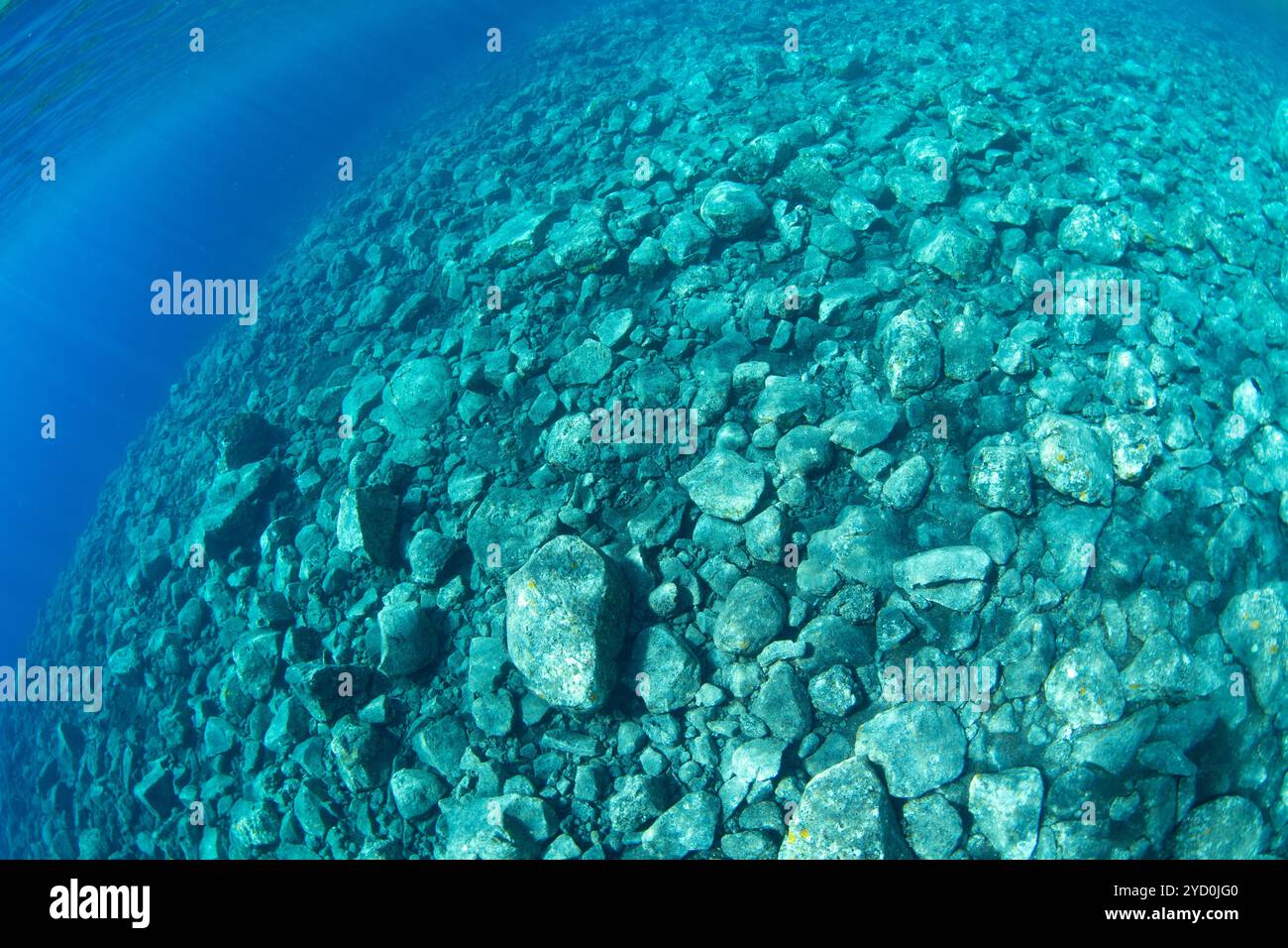 Klares Wasser bedeckt einen flachen Hang vulkanischer Felsbrocken, die von einem abgelegenen Vulkan in Indonesien gestürzt sind. Diese Felsen werden bald von Korallen bedeckt sein. Stockfoto