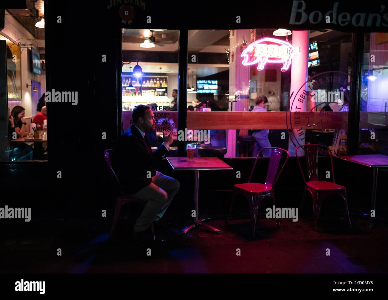 Ein Mann, der allein vor einem Bodean's BBQ sitzt, entlang der Poland Street, im Herzen von Londons Soho, England, Großbritannien Stockfoto