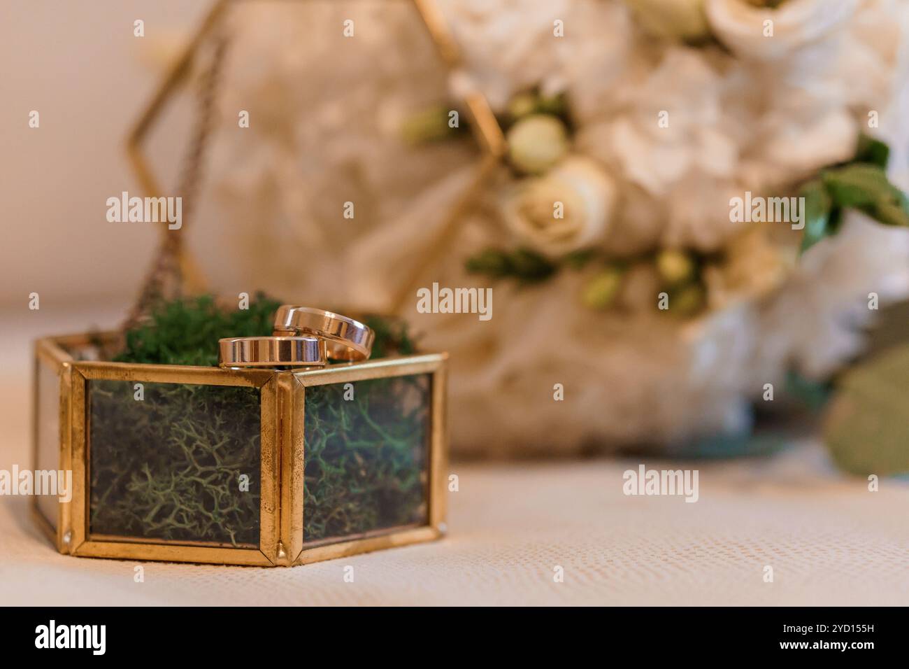 Elegante Hochzeitsringe, die in einer stilvollen dekorativen Box mit Blumen-Arrangement-Hintergrund dargestellt werden. Stockfoto