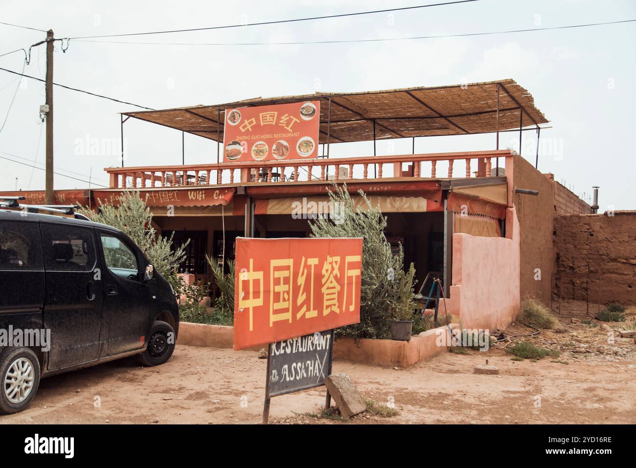 Ein luxuriöses Familienauto parkt neben einem lebhaften marokkanischen Restaurant mit Sitzbereich im Freien. Die Fassade des Hauses zeigt eine besondere Note Stockfoto