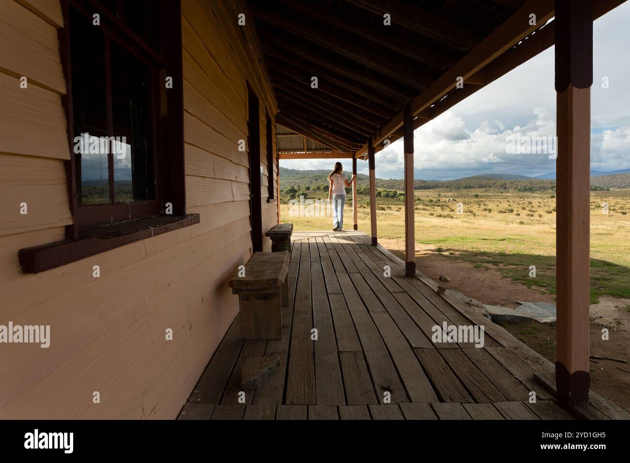 Frau, die auf der Veranda eines ländlichen Holzhofes in verschneiten Hochebenen steht Stockfoto