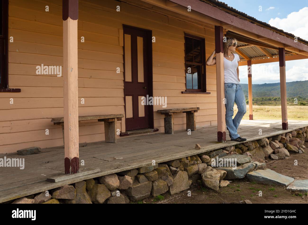 Glückliche, entspannte Frau auf der Veranda eines alten Holzhauses auf dem Land Stockfoto