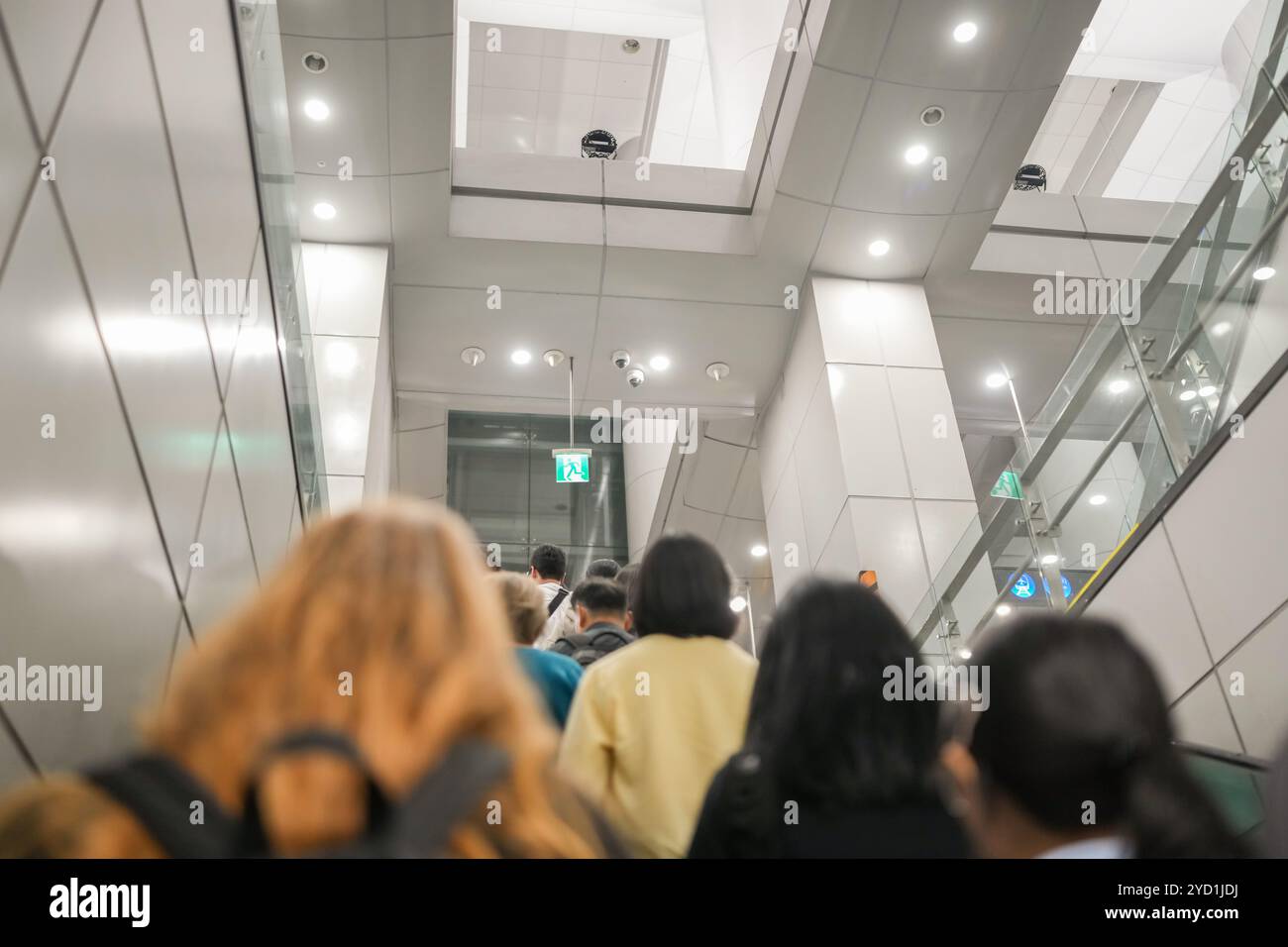 Eine Gruppe von Leuten läuft einen Flur entlang. Einer der Leute trägt einen Rucksack. Der Flur wird durch Deckenleuchten beleuchtet Stockfoto