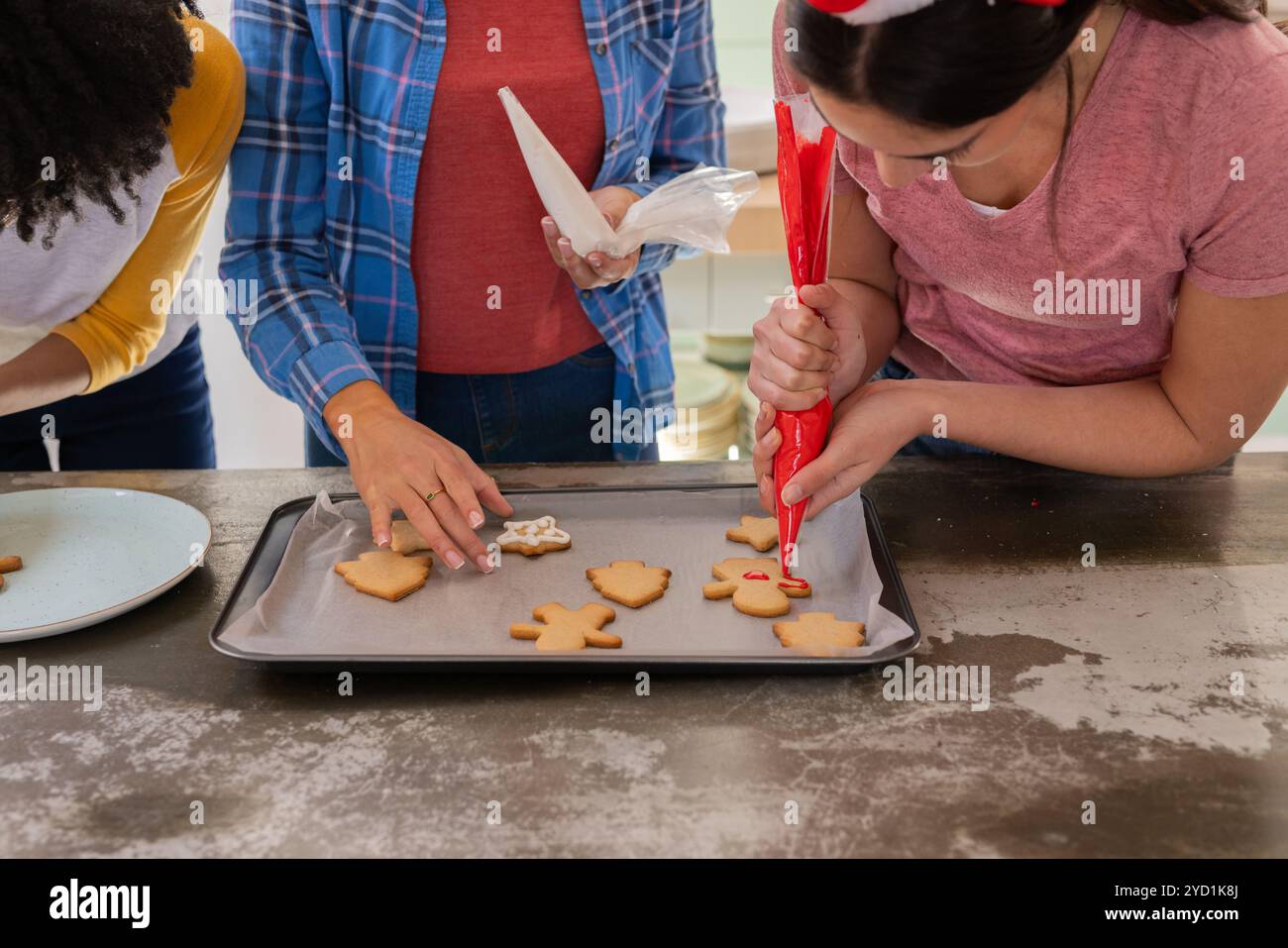 Weihnachtskekse dekorieren, multirassische weibliche Freunde, die festliche Feiertagsaktivitäten teilen, zu Hause Stockfoto