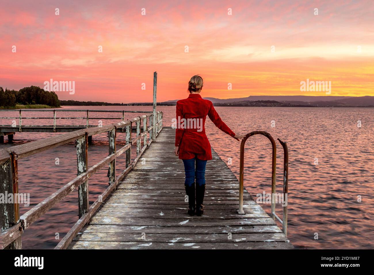 Frau auf rustikalem Holzsteg, die den wunderschönen Sonnenuntergang beobachtet Stockfoto