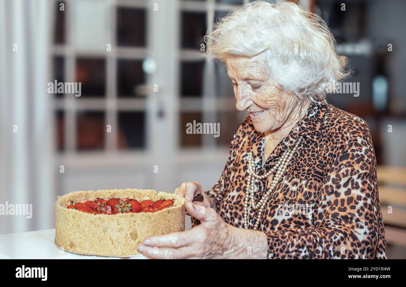 Glückliche Seniorin, die auf ihrer Geburtstagsparty Kuchen schneidet Stockfoto